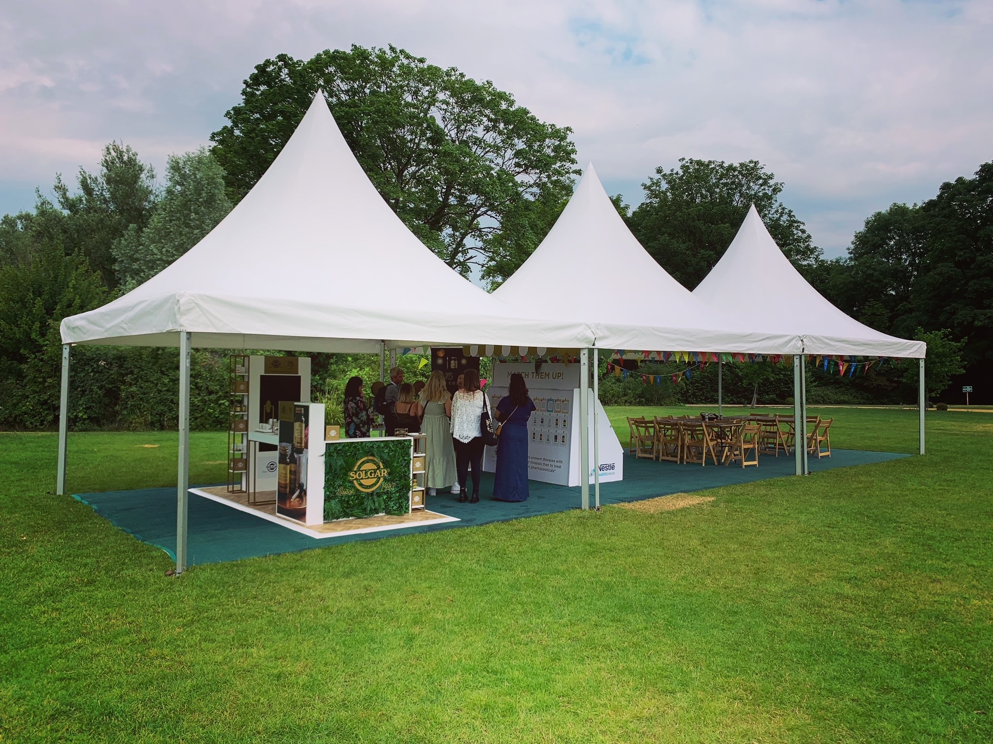 Triple-peaked white pagoda marquee with open sides set on a manicured lawn for a spring garden reception in Surrey