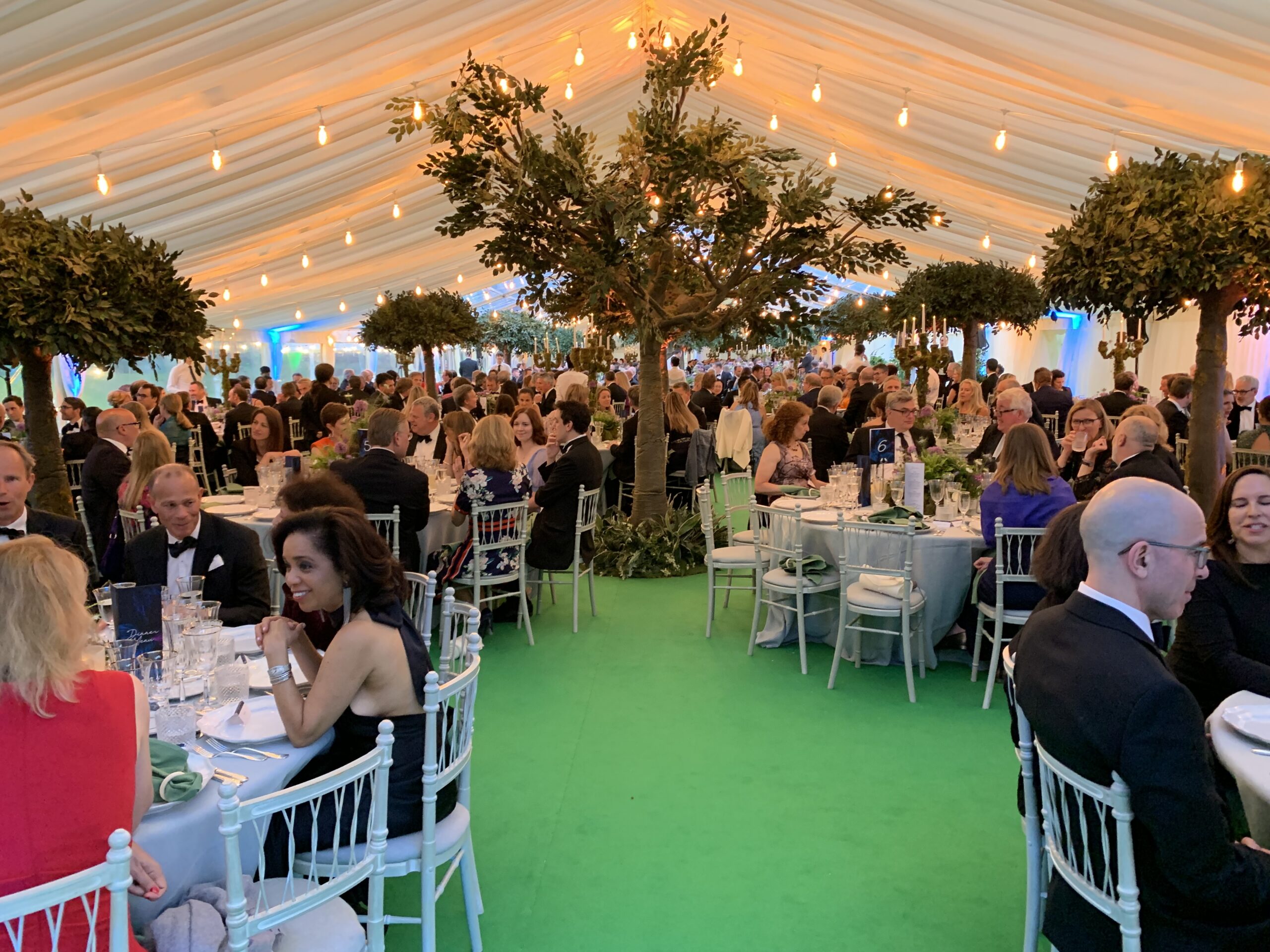Marquee event interior with seated dining, trees, lighting and elegant table settings