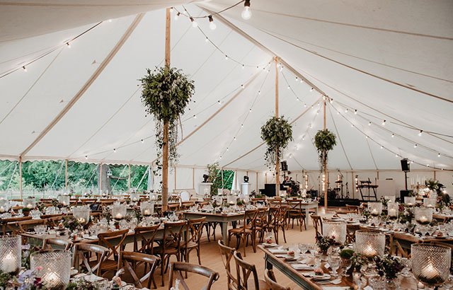 Elegant wedding marquee interior with wooden tables, floral centrepieces and soft festoon lighting in Hampshire