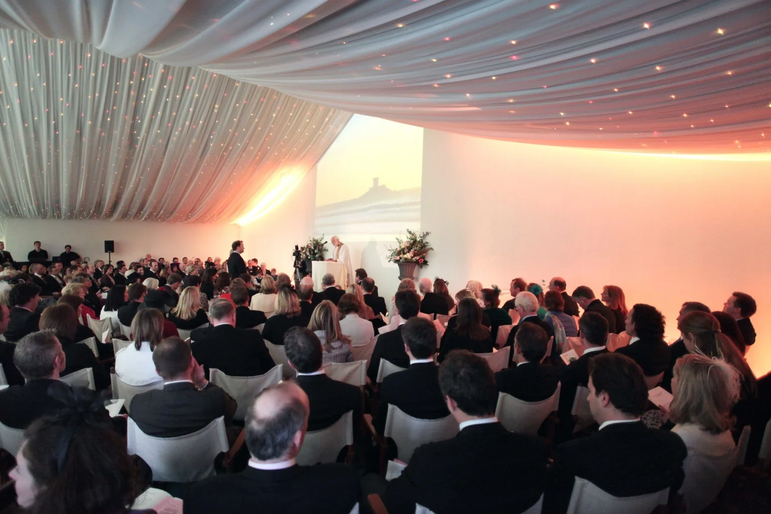 Wedding marquee event with seated guests, draped ceiling and atmospheric lighting